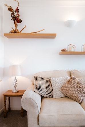 A living room with a sofa, a lamp, a small table, and two wooden shelves with decorative items. - Sea-view Herne Bay Apartment Parking Sleeps 5 (Herne Bay)