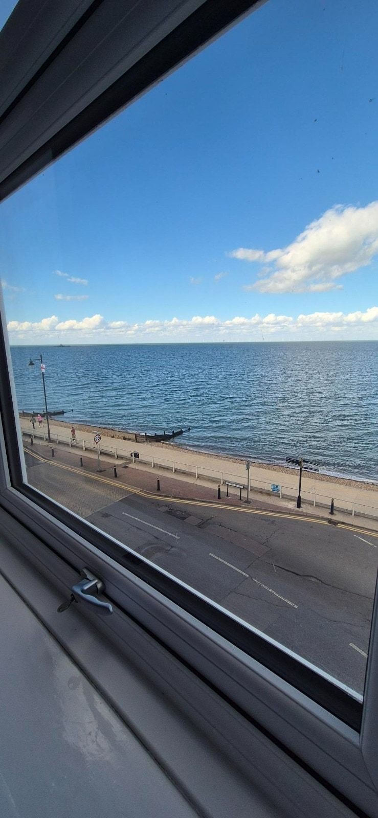 A coastal road with a beach and promenade, viewed from inside a vehicle.