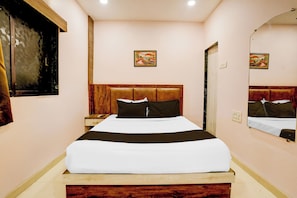 Quarto de hotel com cama, mesa de cabeceira, espelho e duas imagens penduradas na parede.