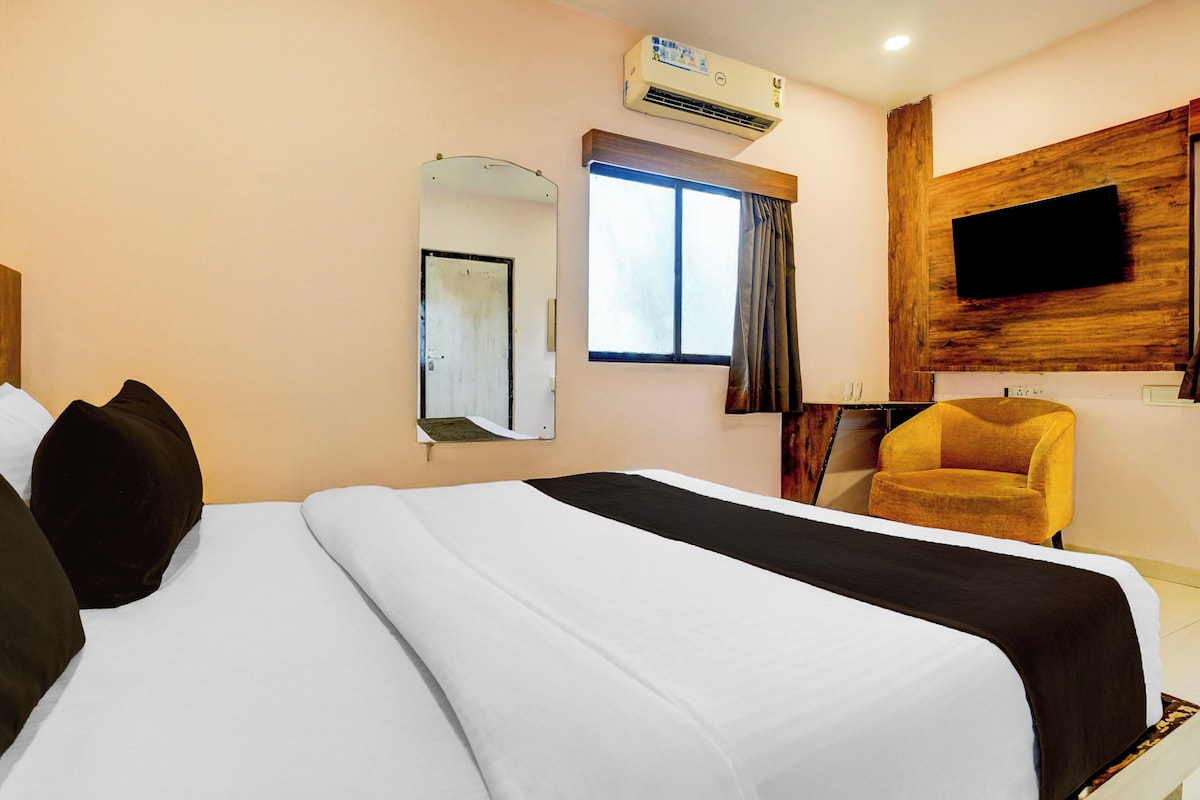 Quarto de hotel com cama, cadeira, televisão fixada na parede e aparelho de ar condicionado.