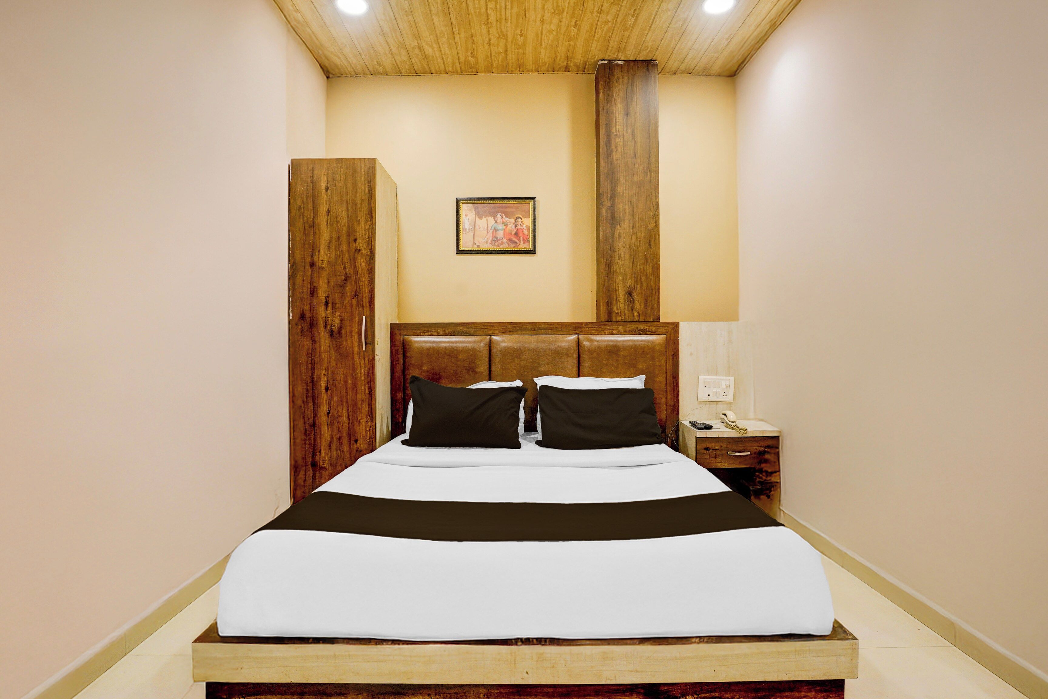 Une chambre à coucher avec une tête de lit en bois, un lit avec une literie blanche et noire, une table de chevet avec un téléphone et un tableau accroché au mur.