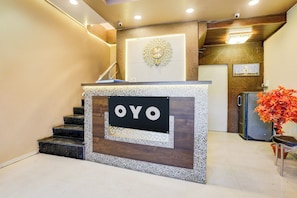 Bancada de recepção com a marca 'OYO', escada com um painel decorativo e um quadro com a imagem de um edifício.