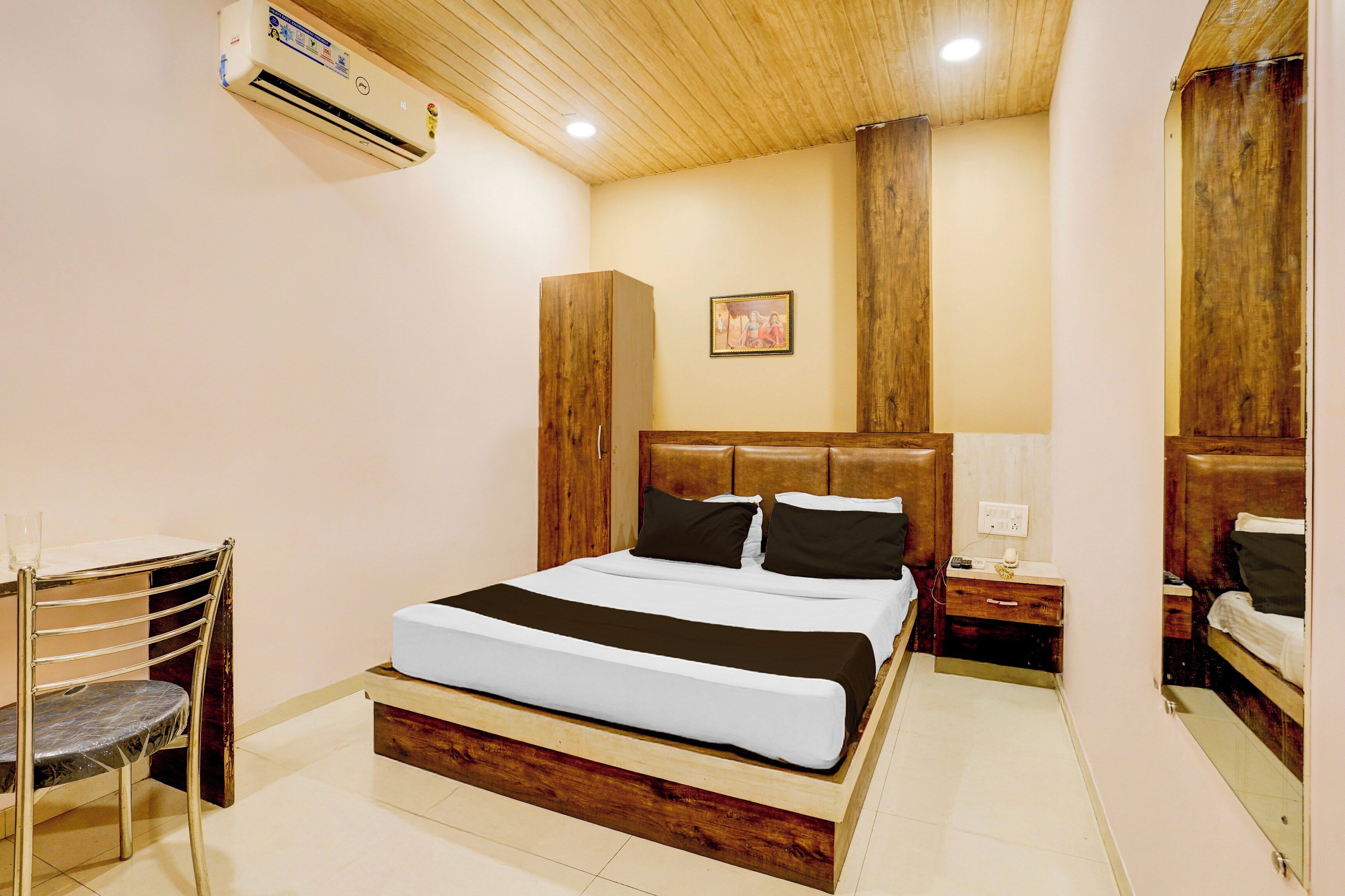 A hotel room with a bed, bedside table, nightstand, and an air conditioning unit.