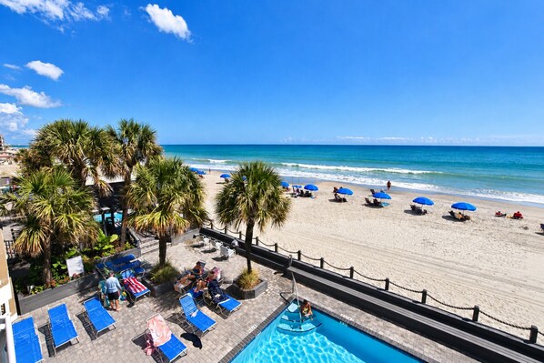 A beachside resort with a pool, lounge chairs, and umbrellas. - Oceanfront 2bed/2bath-Water's Edge Resort-211 Indoor/Outdoor Pool & Hot Tub (Murrells Inlet)