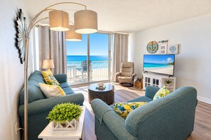 A modern living room with a sofa, armchairs, a coffee table, and a TV. There is a balcony with a view of the sea. - Oceanfront 2bed/2bath-Water's Edge Resort-211 Indoor/Outdoor Pool & Hot Tub (Murrells Inlet)