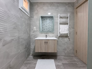 Un baño moderno con pared de mármol, tocador de madera, armario de vidrio para medicamentos y un perchero para toallas.