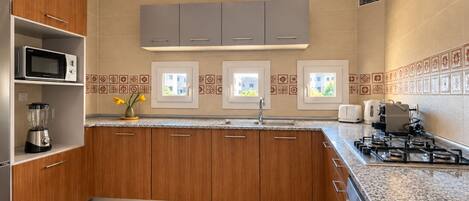A modern kitchen with wooden cabinets, a built-in microwave, a gas stove, and a window with a view of buildings.