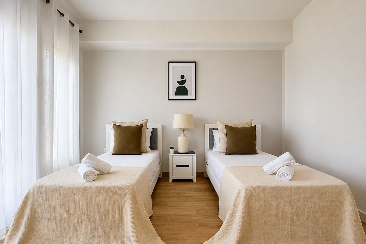 Una habitación de hotel con dos camas, una mesita de noche con una lámpara y un cuadro enmarcado en la pared.