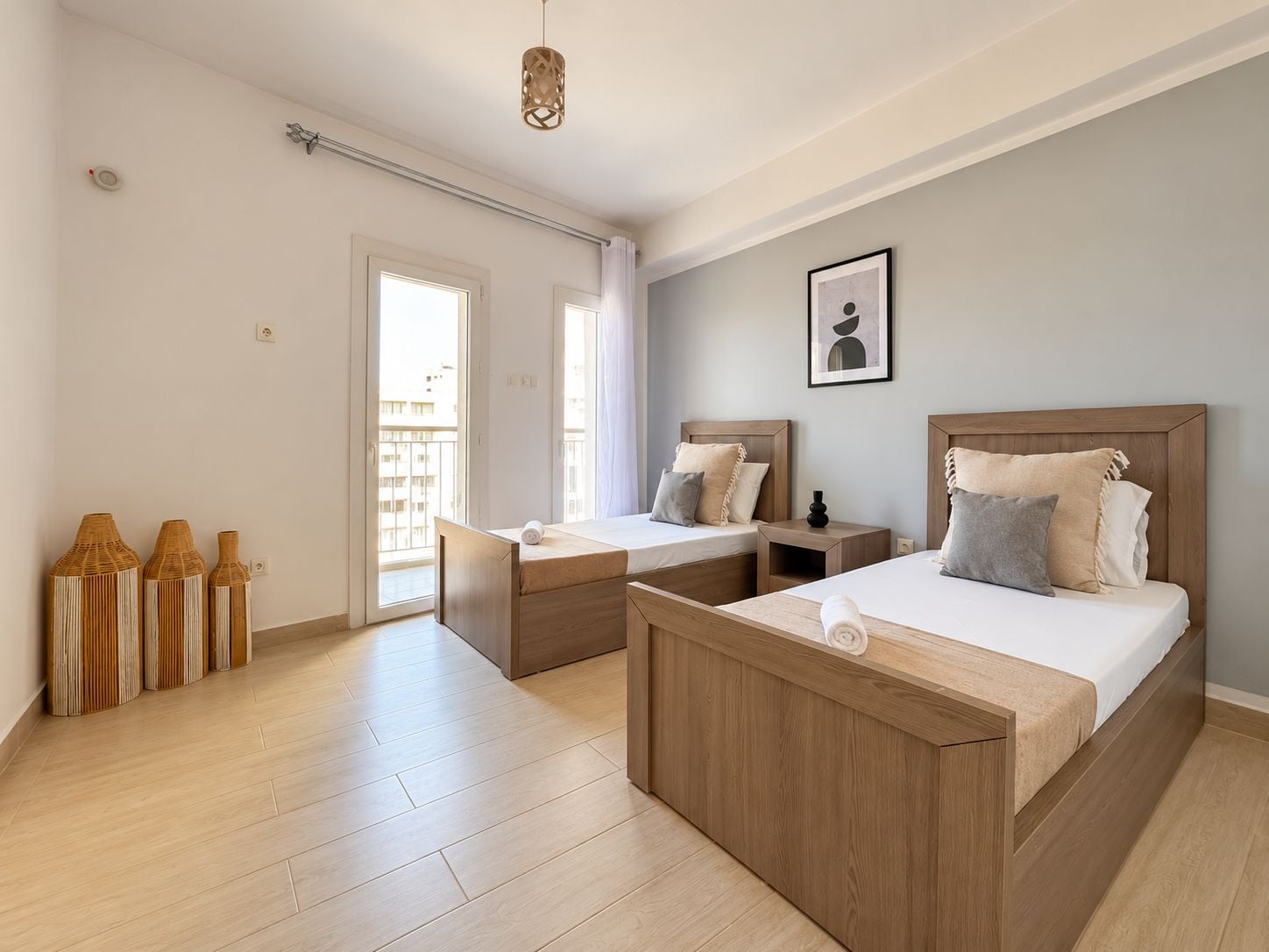A modern bedroom with two beds, a wooden floor, and a large window.