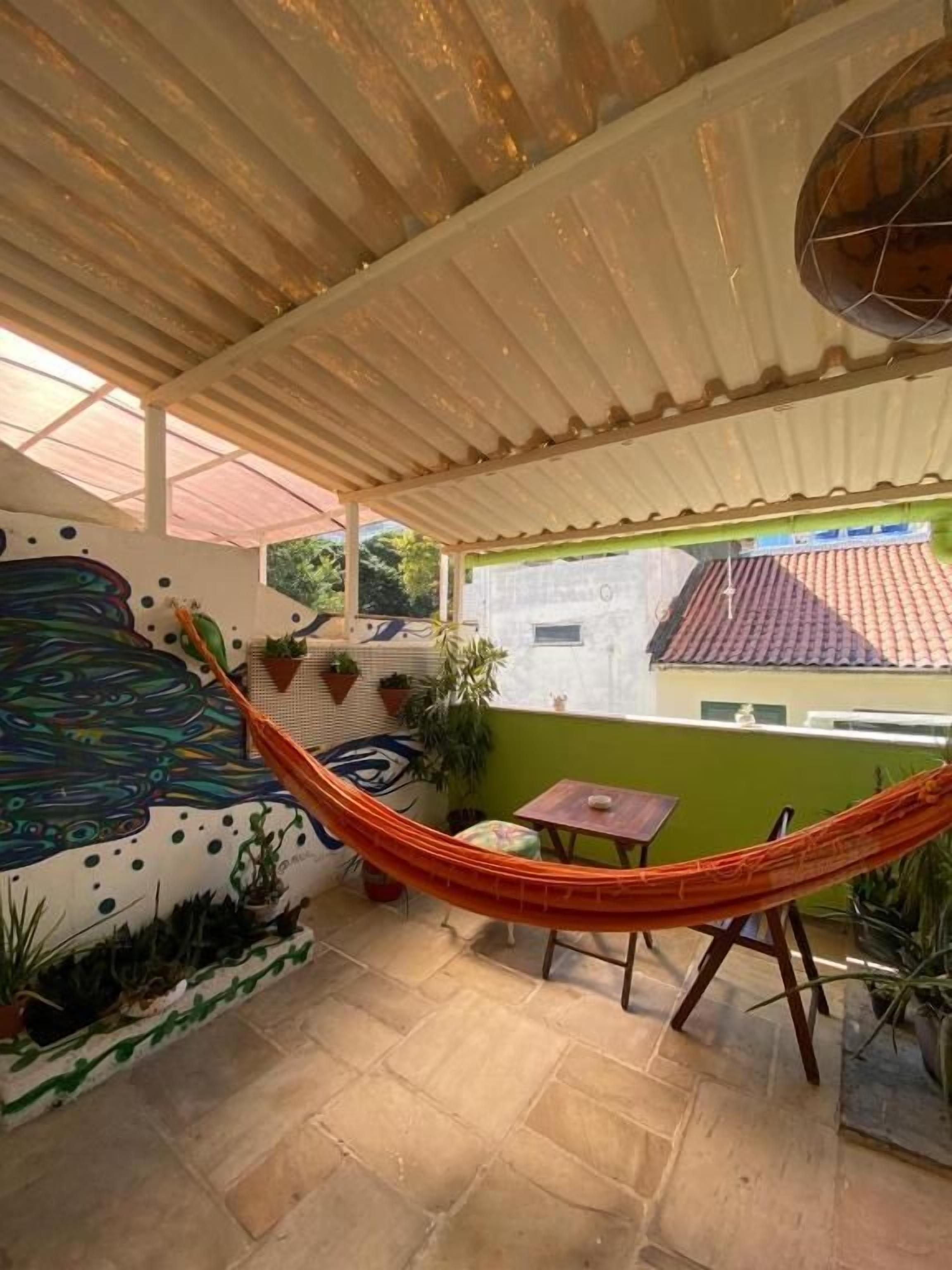 A covered outdoor area with a hammock, a small table, and potted plants.