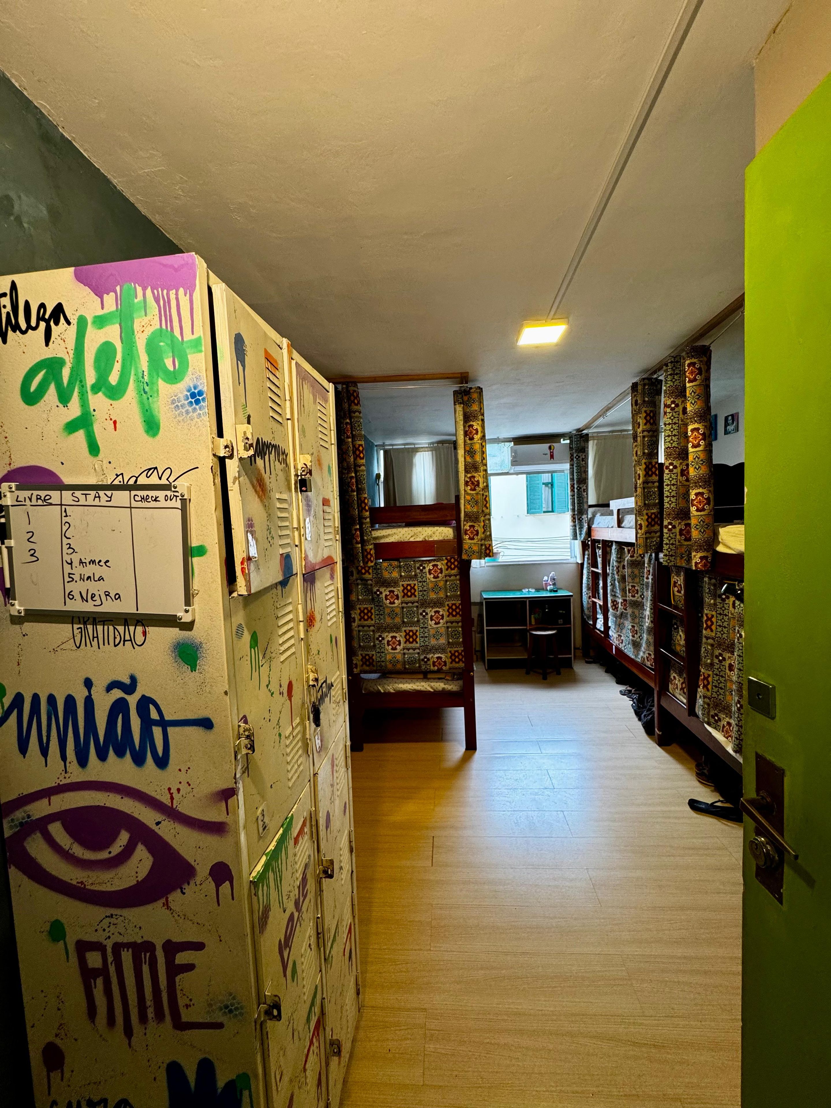 A corridor with lockers, a check-in board, and a bed with patterned curtains.