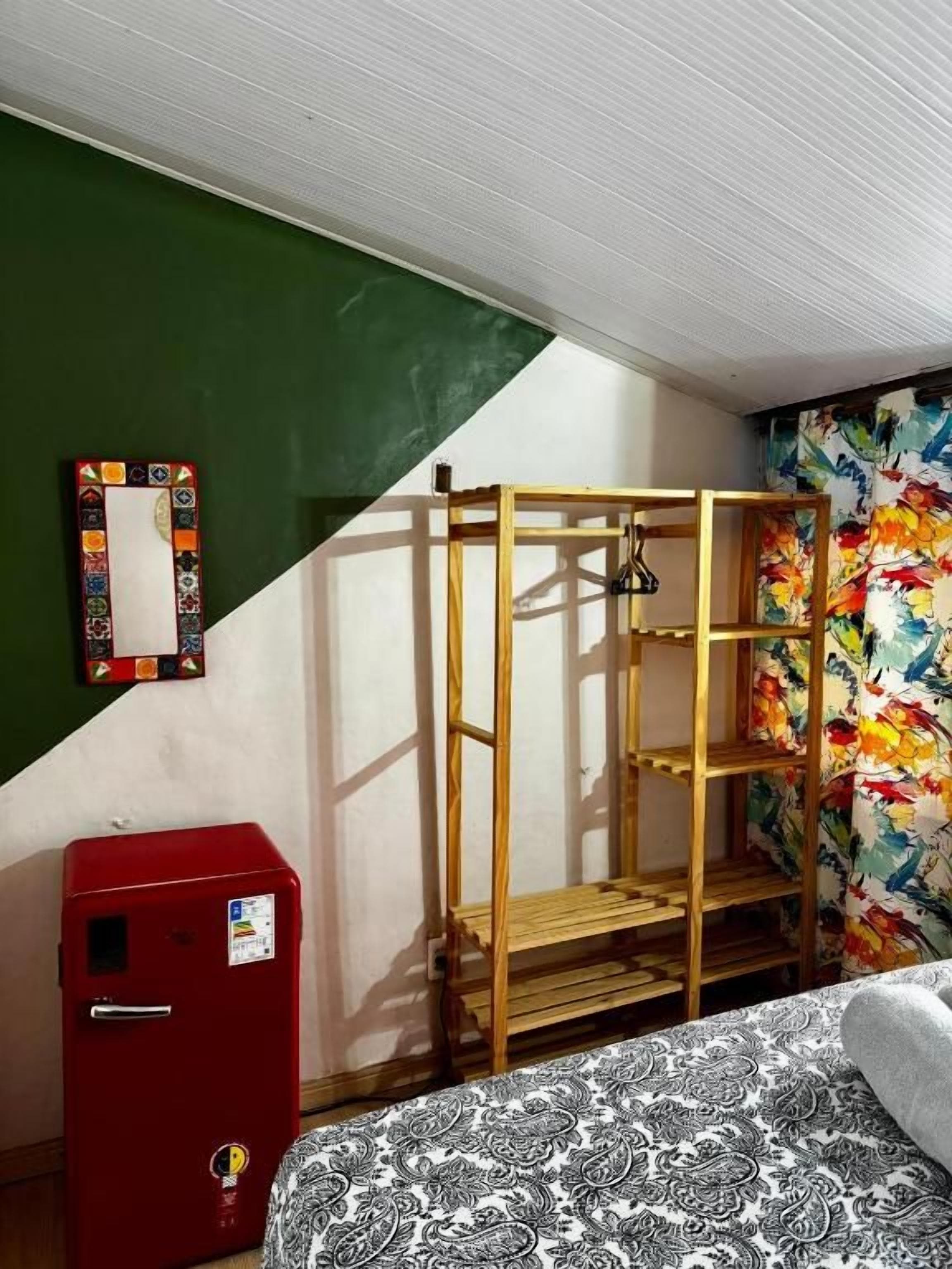 Una habitación con una cama litera, una maleta roja, una escalera de madera y un mural colorido en la pared.
