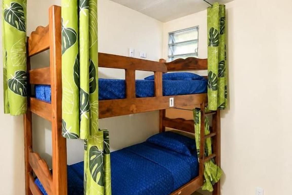 Ein Etagenbett mit grünen Vorhängen und blauer Bettwäsche in einem Zimmer mit Fenster und Fliesenboden.