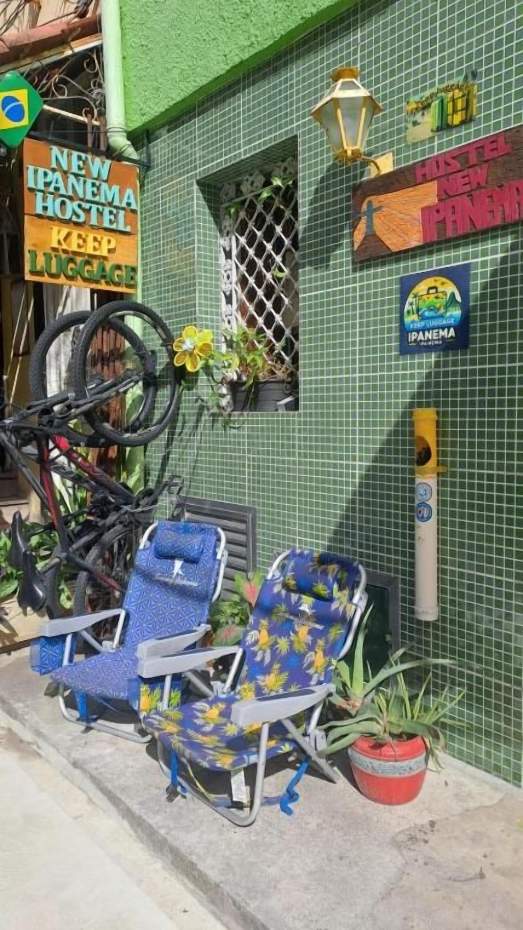 A hostel with a green exterior, a bicycle, and two blue chairs with floral patterns.