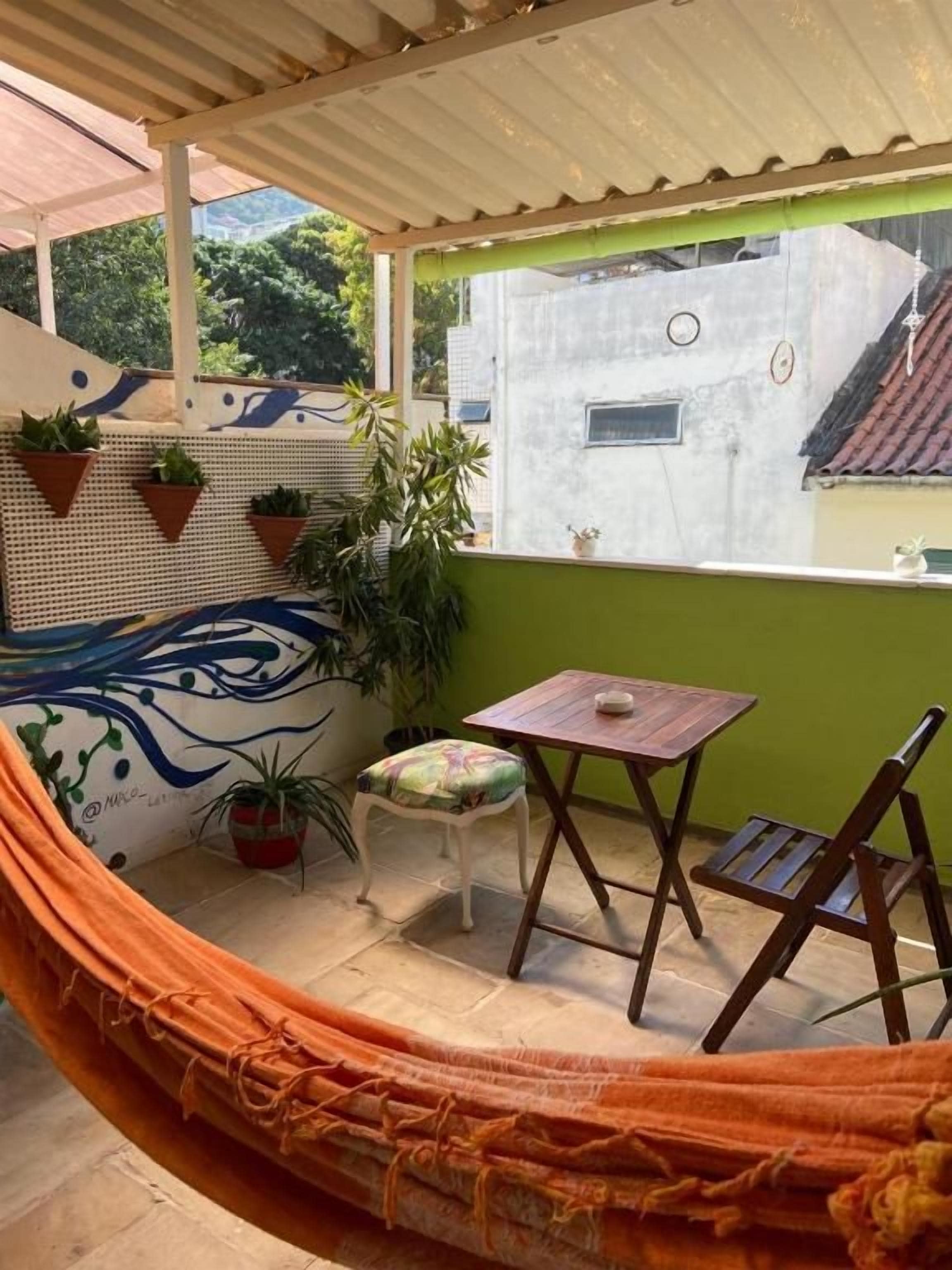 A hammock, a small table, a chair, and potted plants in a covered outdoor area.