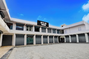 A modern hotel with a flat facade, multiple closed shutters, and a clear blue sky. - Super Hotel O Greater Noida West Link (Greater Noida)