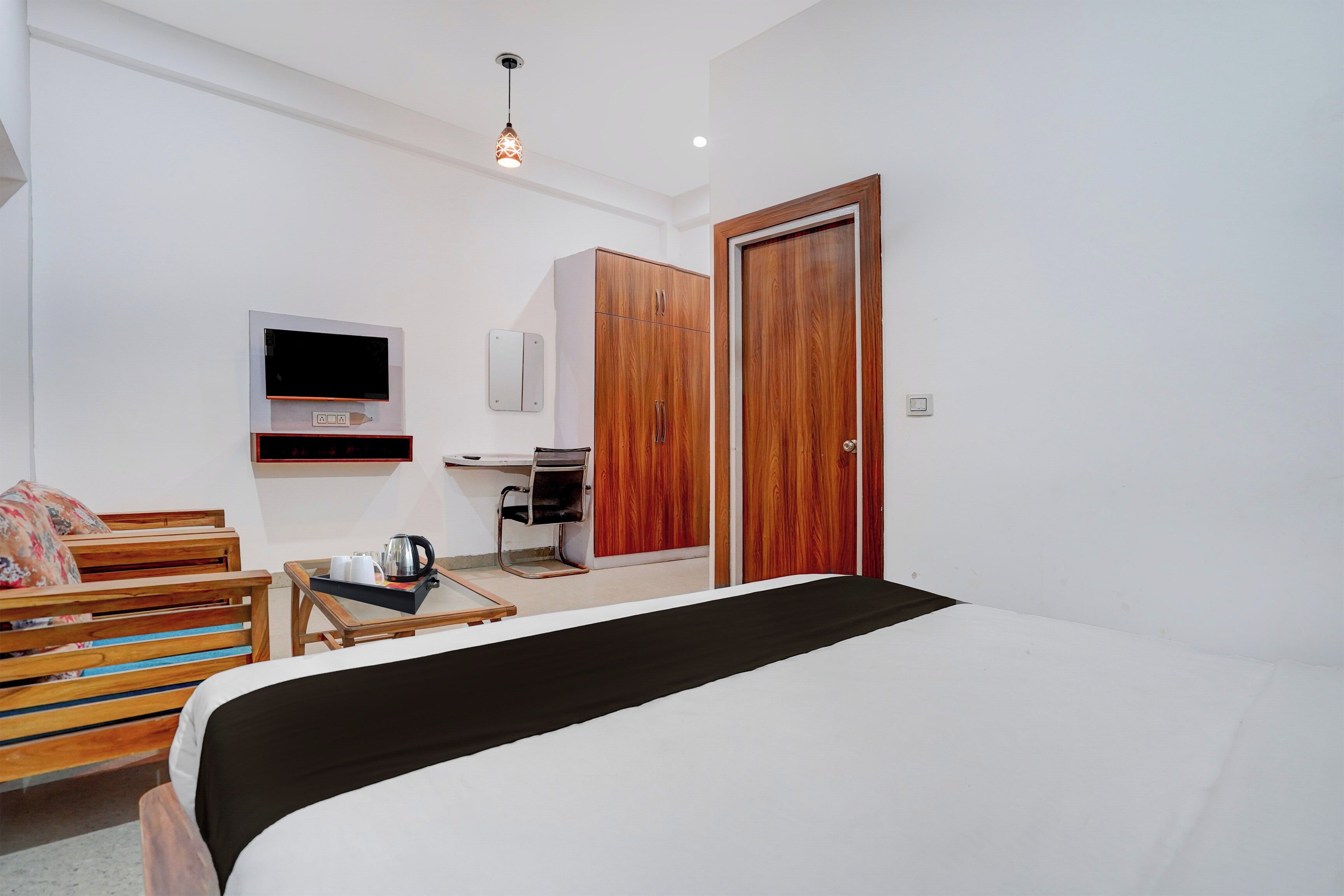 Una habitación de hotel con una cama, un armario de madera, un televisor montado en la pared, una mesita con una tetera y una silla.