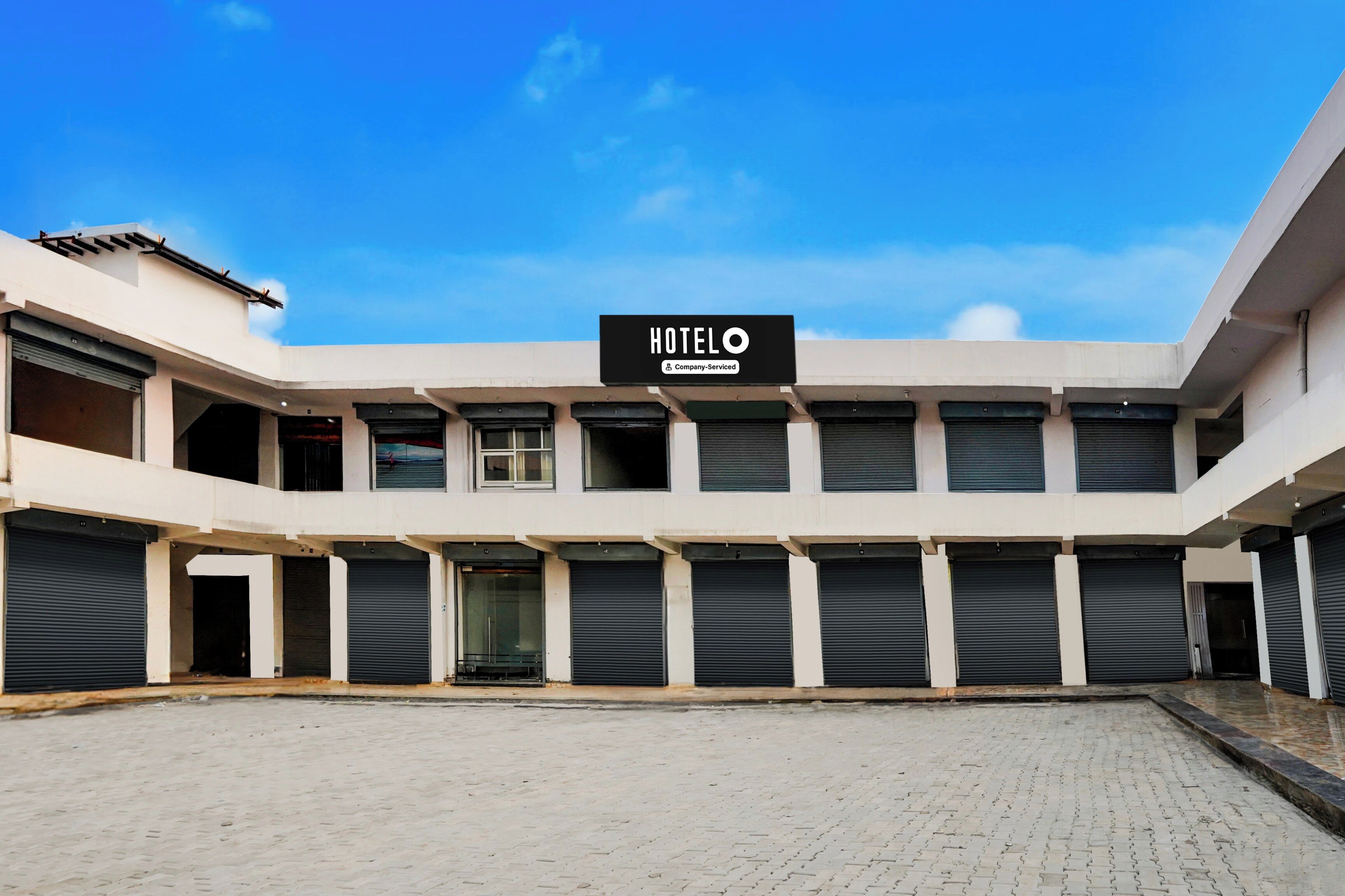 Un hotel con un letrero, varias persianas cerradas y un patio empedrado.