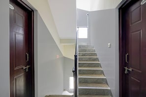 Una escalera con barandilla que lleva a un rellano, flanqueada por dos puertas de madera oscura con una placa numérica.