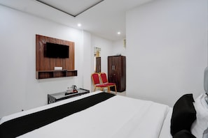 Habitación de hotel con cama, televisor montado en la pared, armario y zona de estar con sillones.