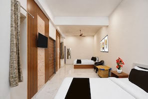 A hotel room with a bed, a flat-screen TV, a ceiling fan, and a small table with a vase of flowers. - Hotel O Khatu Shyam Temple (Danta Ramgarh)