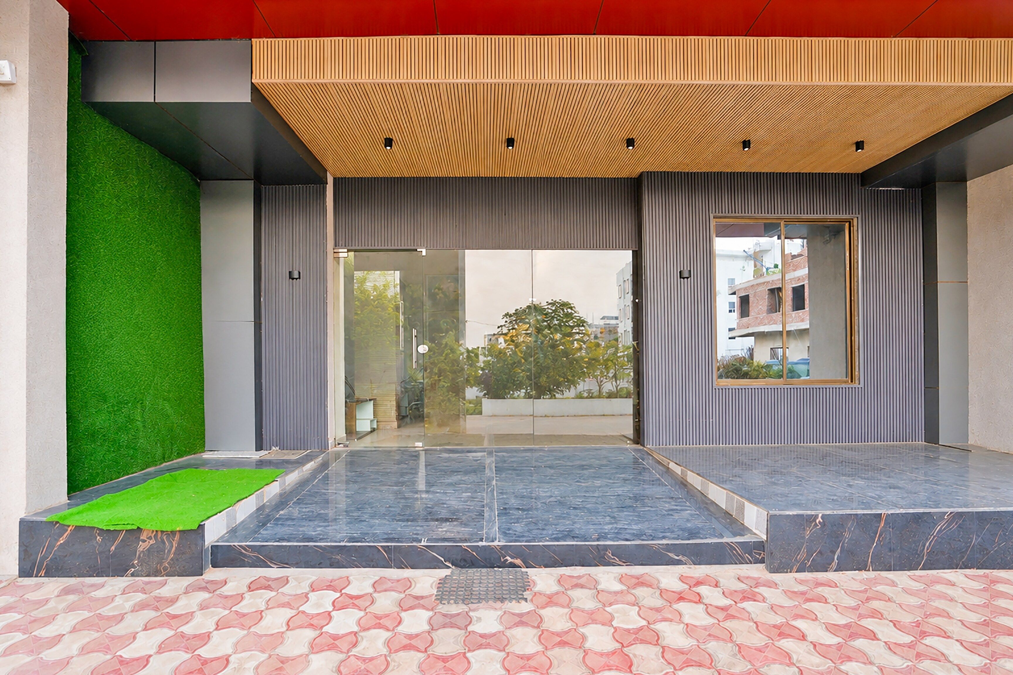A modern building entrance with a glass door, a green artificial grass area, and a tiled floor.