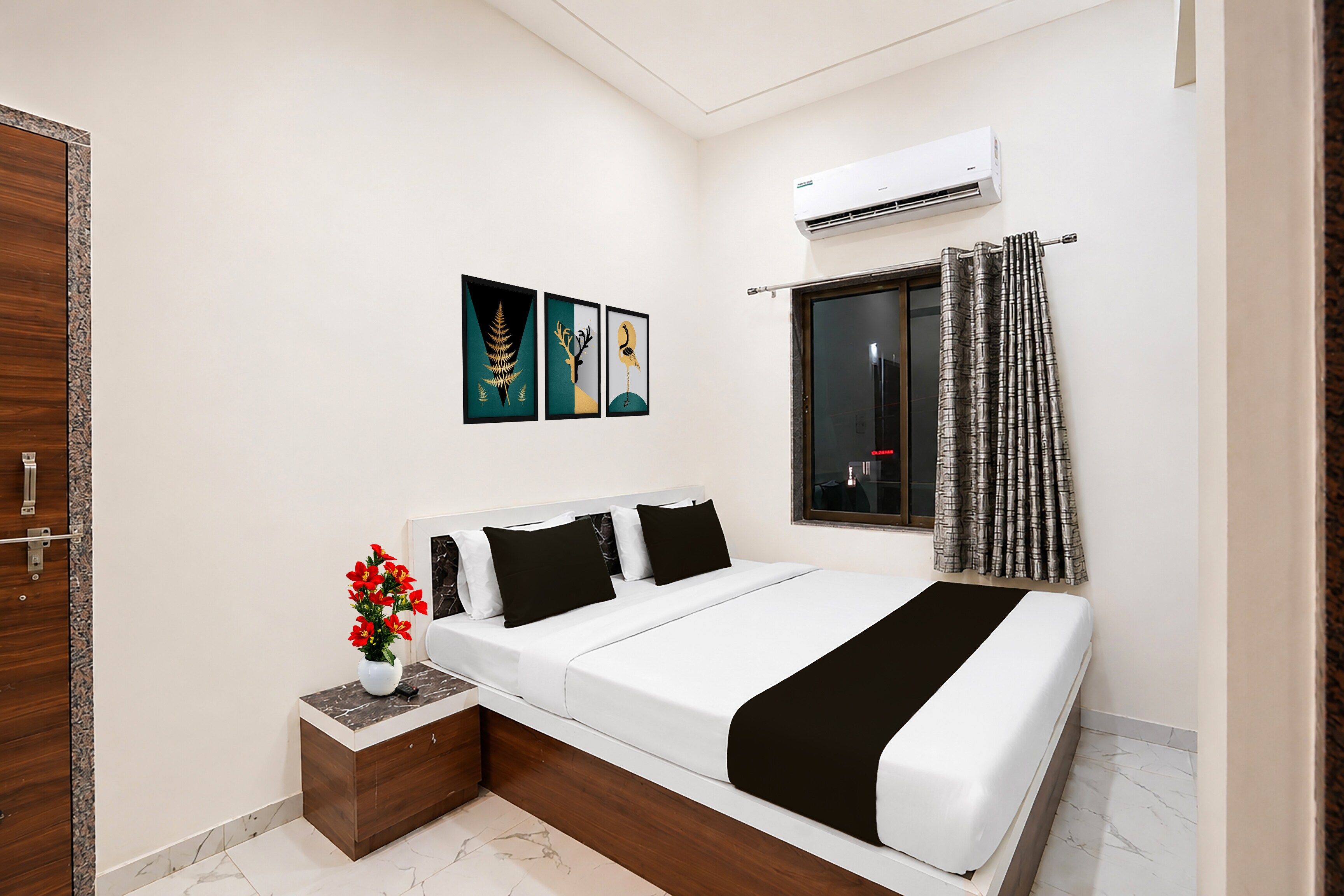 Un dormitorio con cama, mesita de noche, un jarrón de flores y una ventana con cortinas.