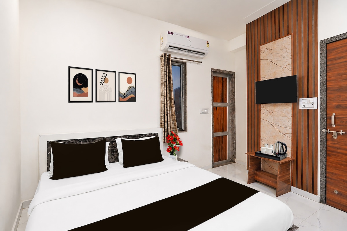 A hotel room with a bed, a TV, a window with curtains, and artwork on the wall.