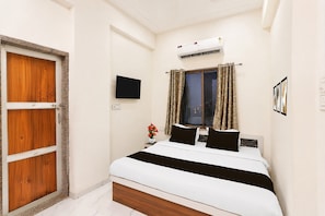 A bedroom with a bed, a wooden door, a wall-mounted TV, an air conditioner, and a window with curtains. - Hotel O Khatu Shyam Temple (Danta Ramgarh)