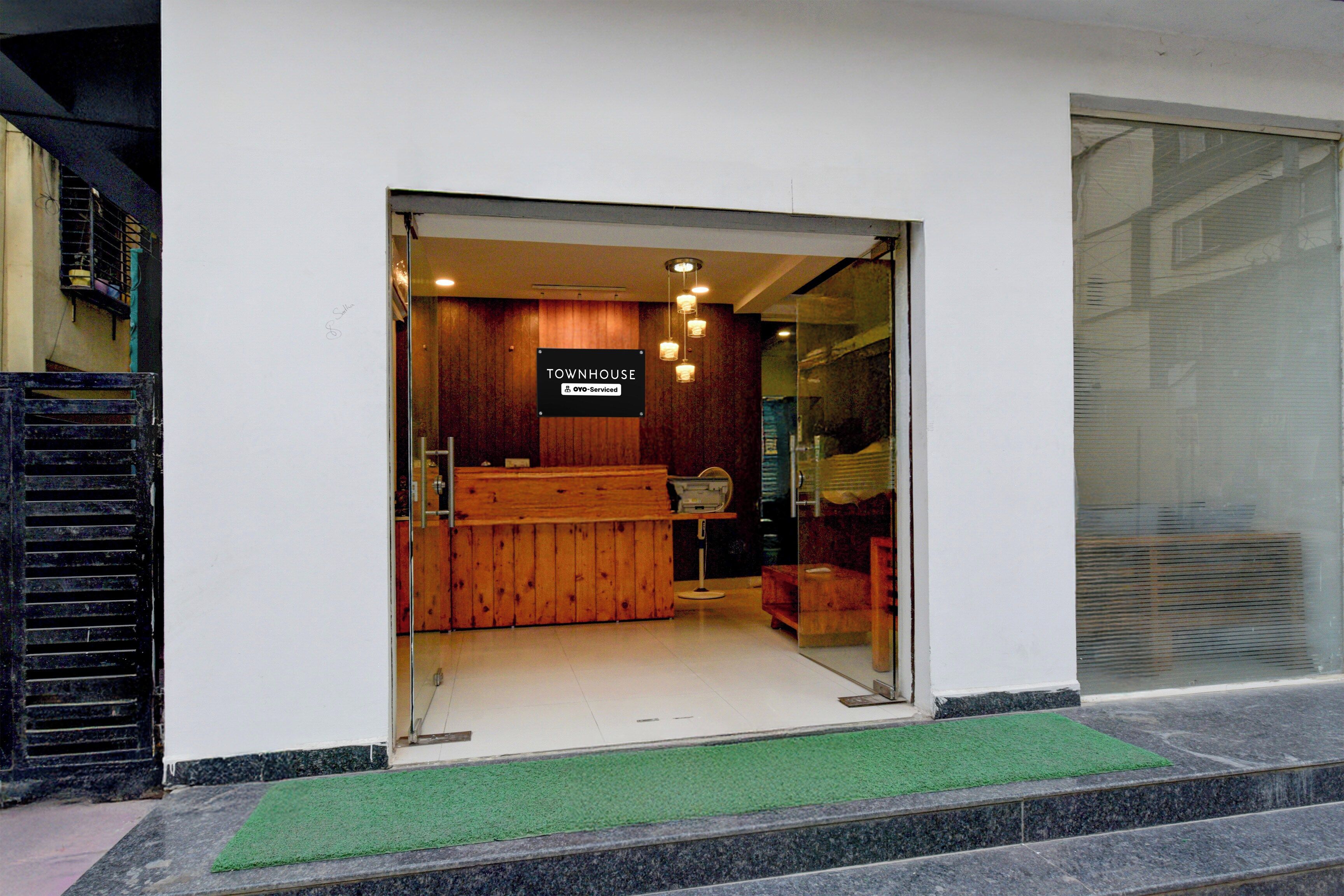 A reception area with a wooden reception desk, a sign indicating it is serviced by OYO, and a glass door entrance.