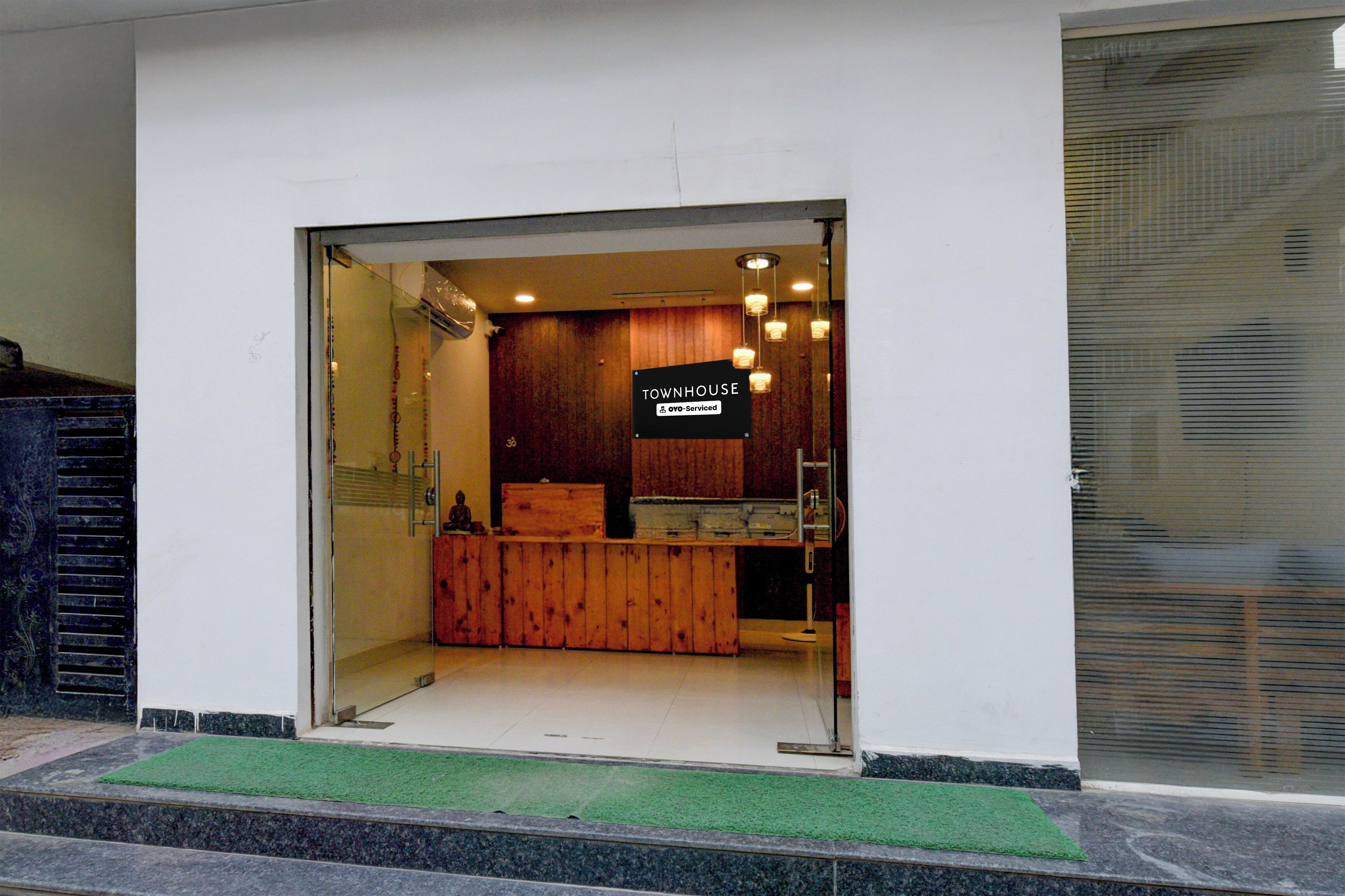 A hotel entrance with a reception desk, a sign indicating it is a 'TOWNHOUSE' and 'Yoyo-Serviced', and a small Buddha statue on the counter.