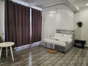 Un dormitorio con cama, mesita de noche, silla, ventilador y ventana con cortinas.