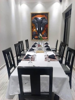 Un comedor con una larga mesa dispuesta para cuatro personas, rodeada de sillas negras, y una obra de arte enmarcada en la pared.