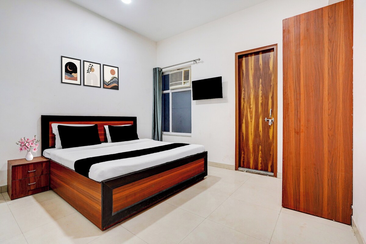 A bedroom with a bed, a nightstand, a wall-mounted TV, and a wooden door.