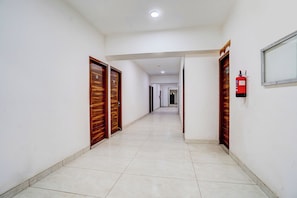 A corridor with wooden doors, a fire extinguisher, and a tiled floor. - Hotel O Sector 49 Noida (Noida)