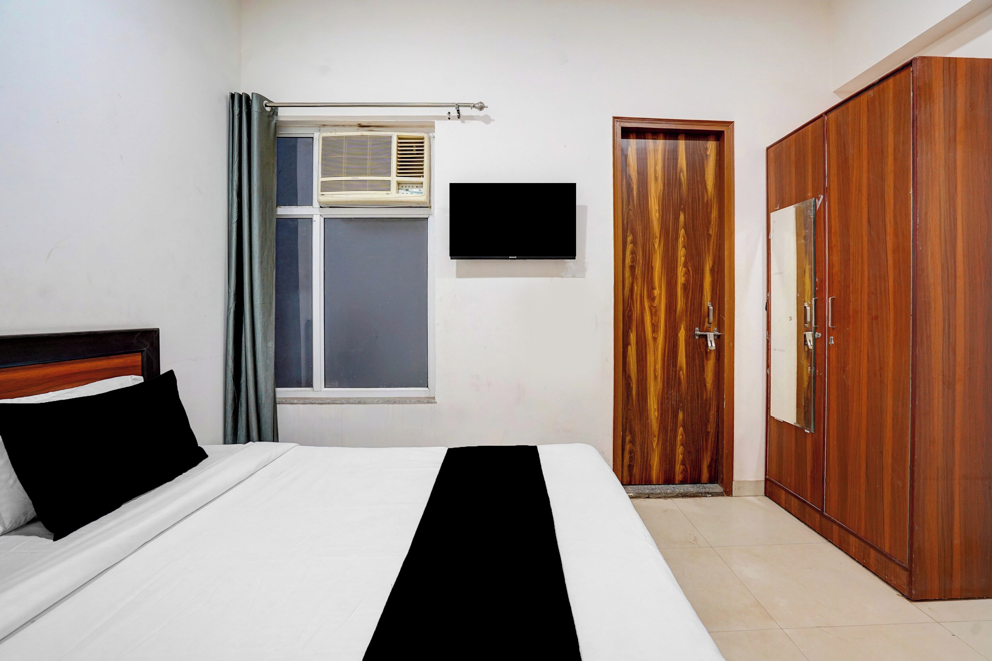 A bedroom with a bed, a wardrobe, a television, and a window with curtains.