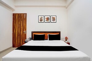 A hotel room with a wooden door, a bed with black and white bedding, a nightstand with a coffee pot, and three framed pictures on the wall. - Hotel O Sector 49 Noida (Noida)