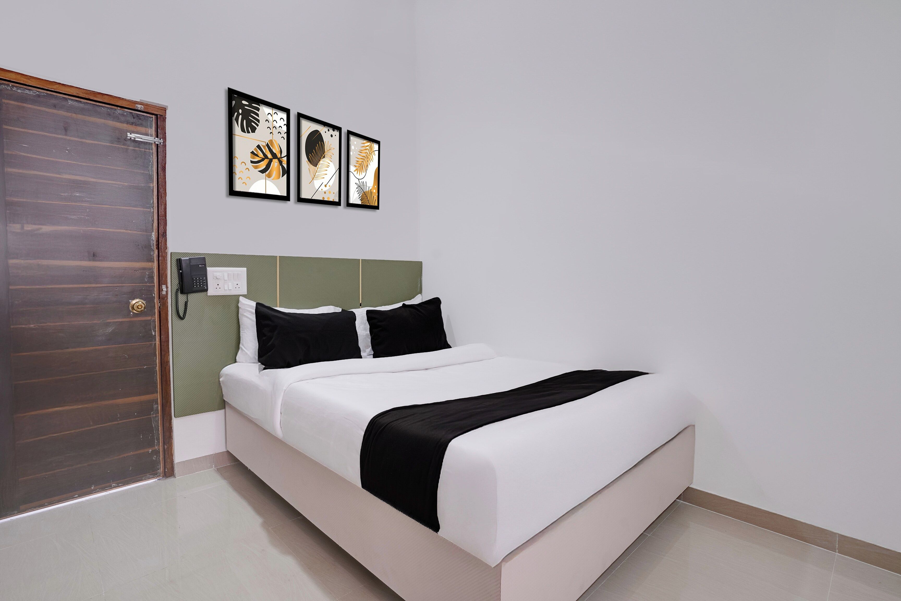 Una camera d'albergo con un letto, una porta, un telefono fissato al muro e tre opere d'arte incorniciate.