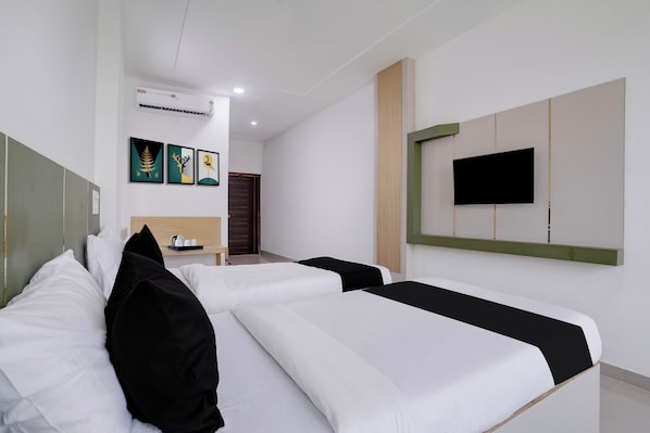 A hotel room with two beds, a flat-screen TV mounted on the wall, and a small table with a kettle and cups.