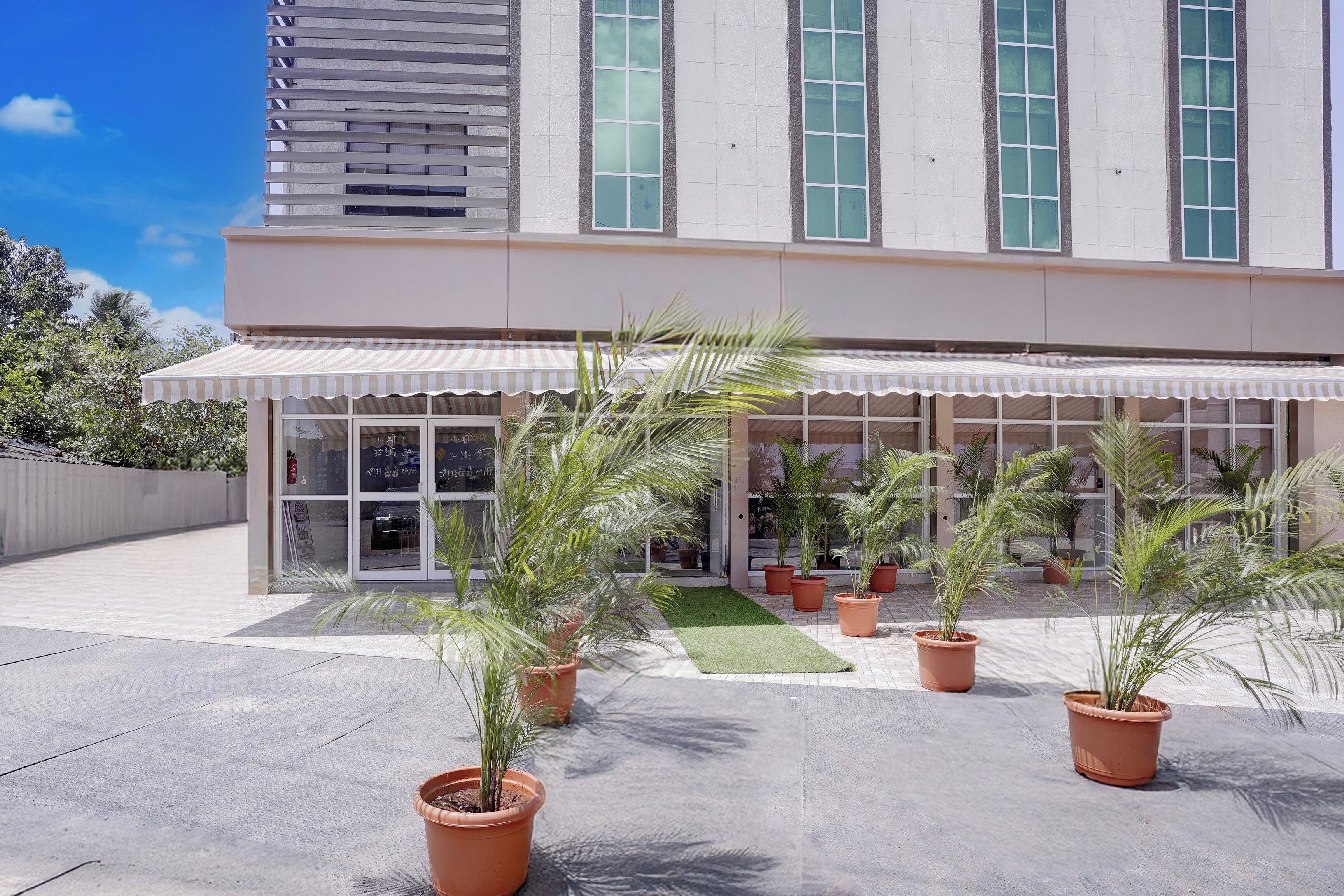 A modern building with a covered entrance, potted plants, and a clear sky.