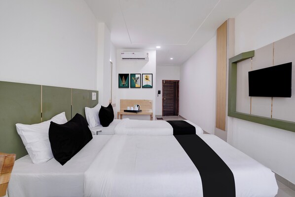 A hotel room with a large bed, a bedside table with a kettle, and a flat-screen TV mounted on the wall.