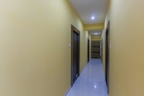 A long, narrow hallway with doors on both sides, leading to a gated area at the end. - Hotel O Prime International (Baruipur)