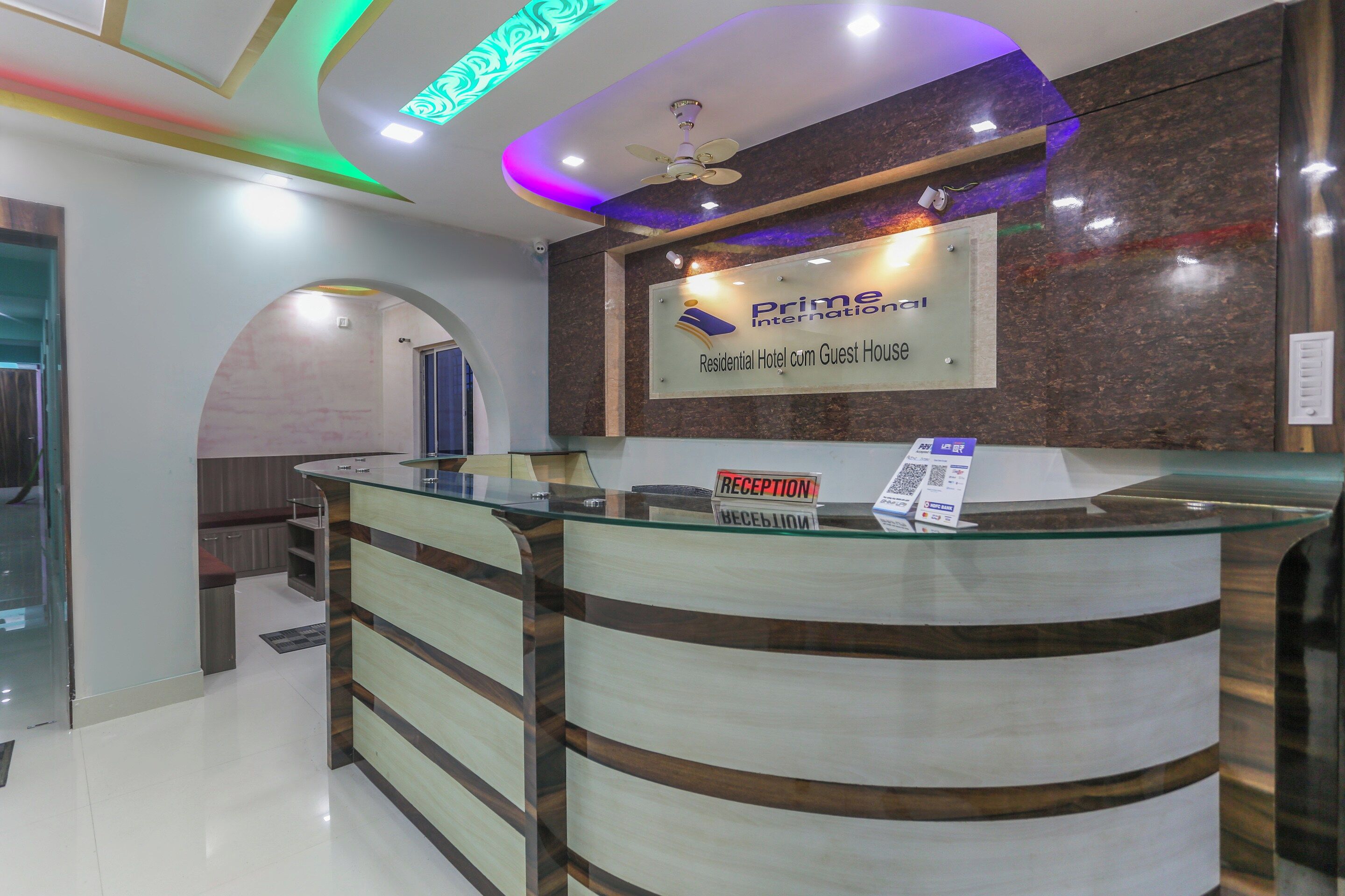 A reception desk with a sign for Prime International, a ceiling fan, and a reception area with a glass partition.