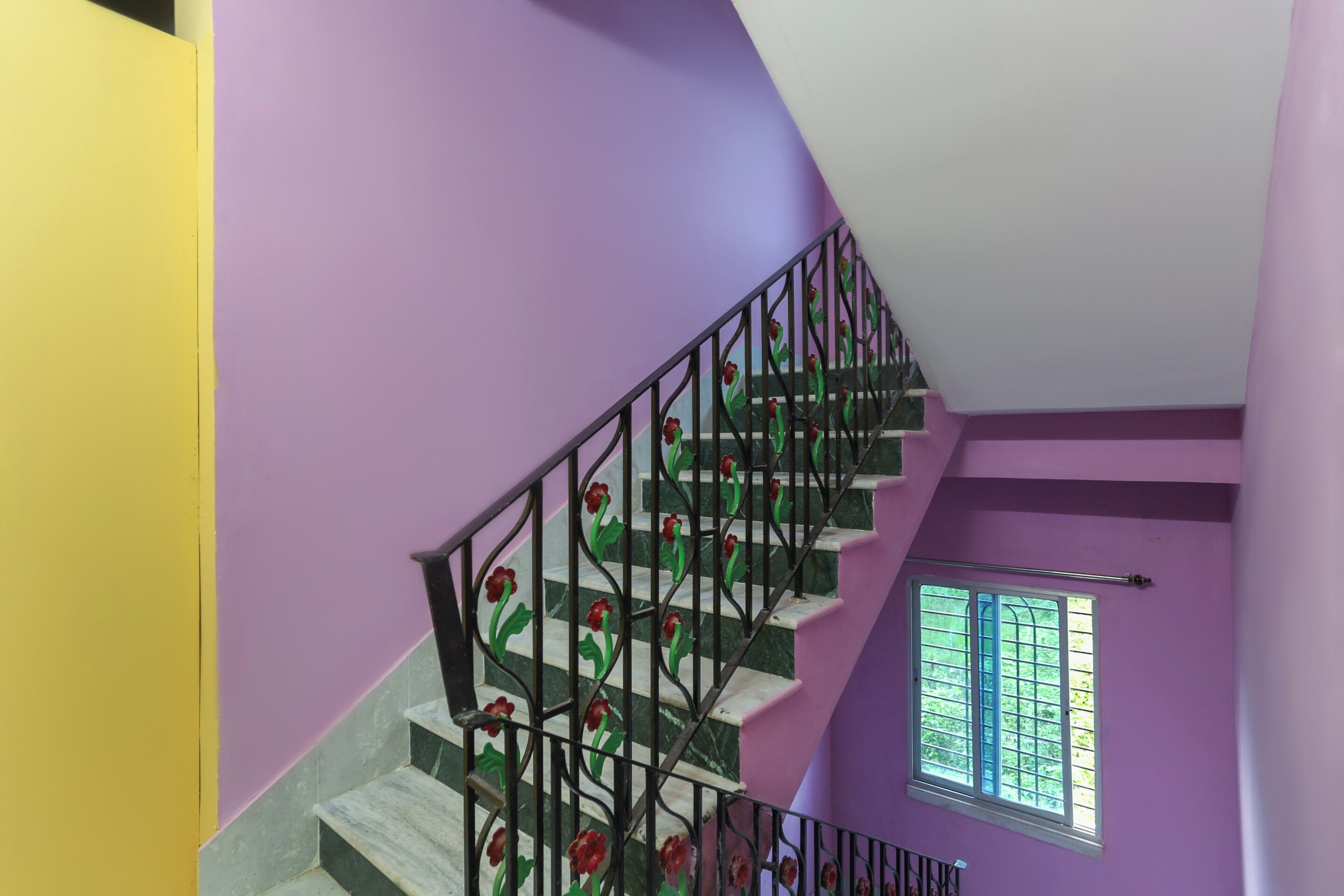 Una escalera con una pared morada y un ventanal con vistas al verdor.