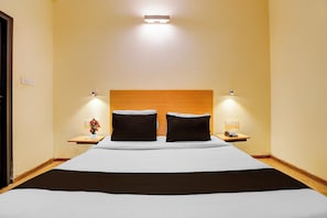 A hotel room with a large bed, two bedside tables, a nightstand, and a wall-mounted light fixture. - OYO Townhouse Singapore Mall (Lucknow)