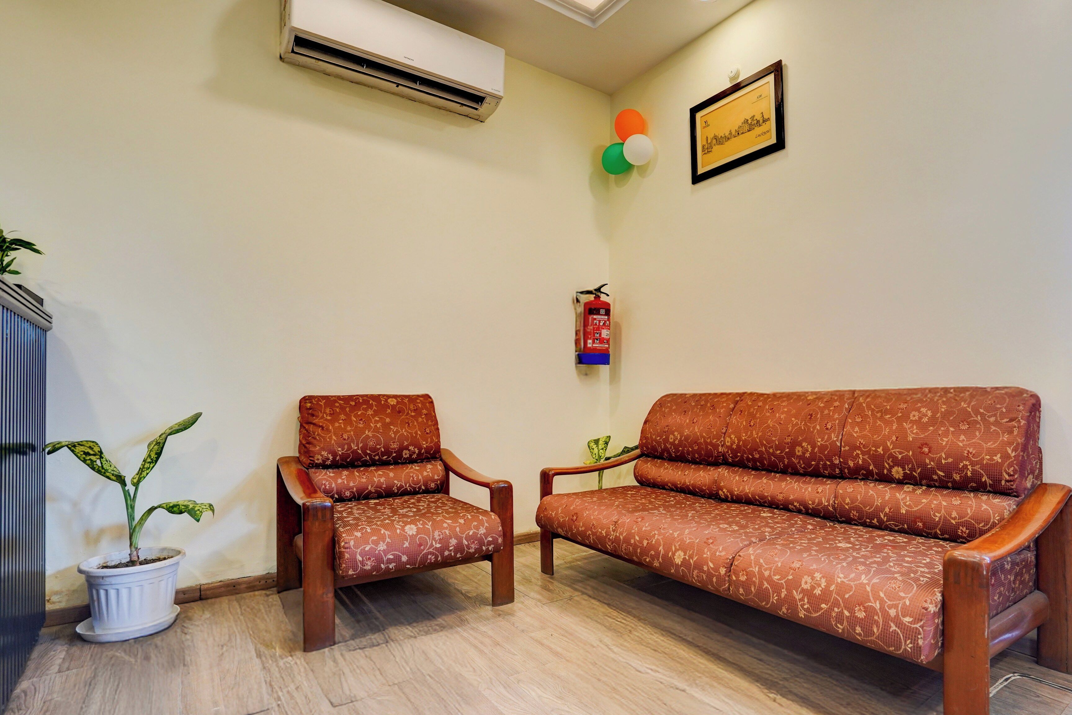 A room with a sofa and two chairs, a potted plant, an air conditioning unit, a framed picture, and a fire extinguisher.