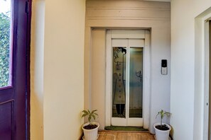 Un passadís amb una porta blanca, un panell de vidre amb una silueta negra, i dues plantes en testos a cada costat.