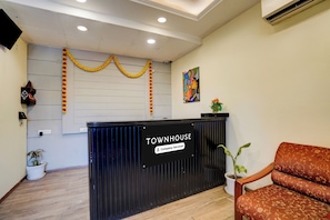 A reception desk with a sign reading 'TOWNHOUSE Company-Serviced.' There is a chair to the right and a wall-mounted painting above the desk. - OYO Townhouse Singapore Mall (Lucknow)