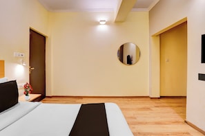 Ein Hotelzimmer mit einem Bett, einem runden Spiegel, einem Nachttisch mit Lampe und einem kleinen Tisch mit Blumen.