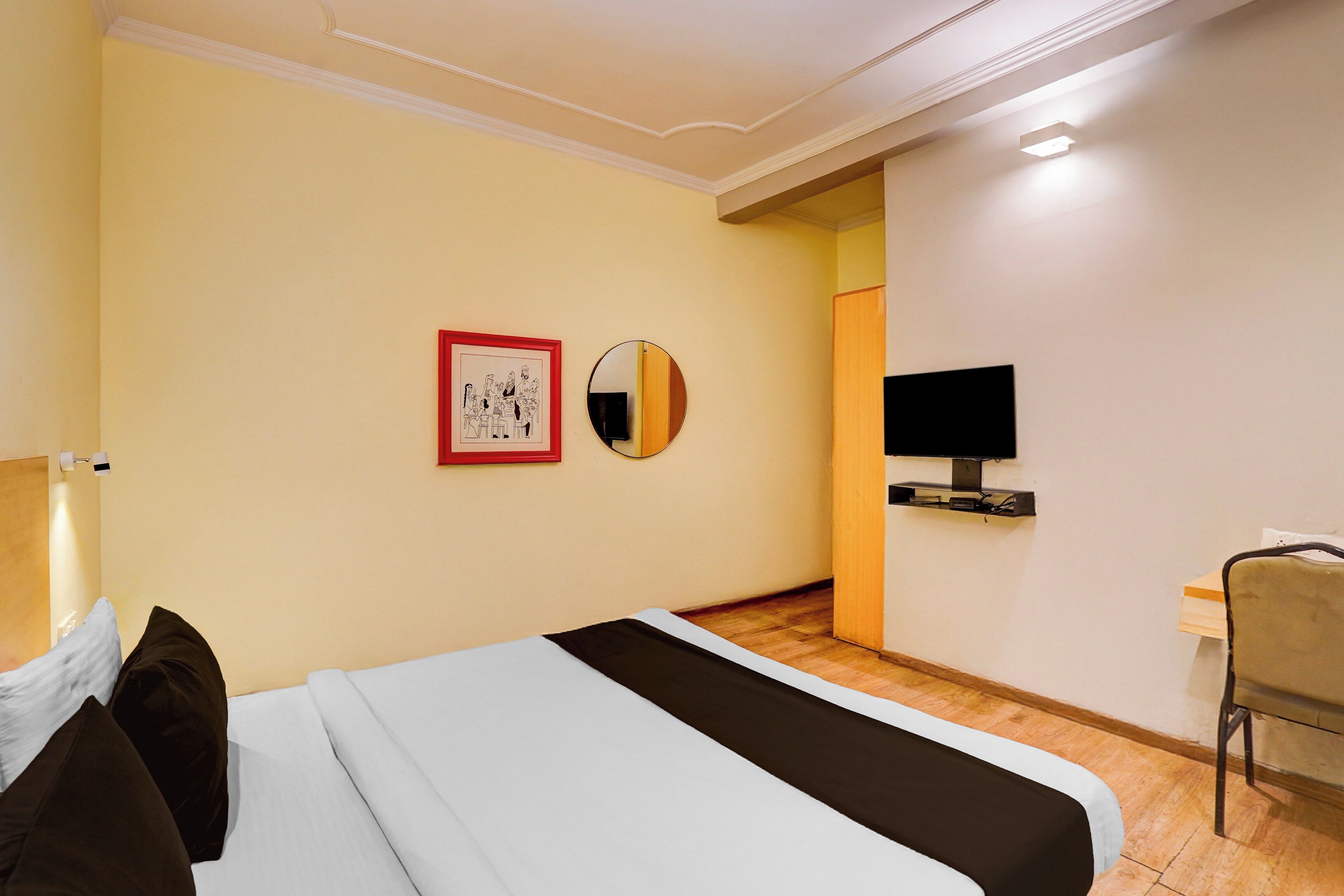 A hotel room with a bed, a desk, a television, and a framed picture on the wall.
